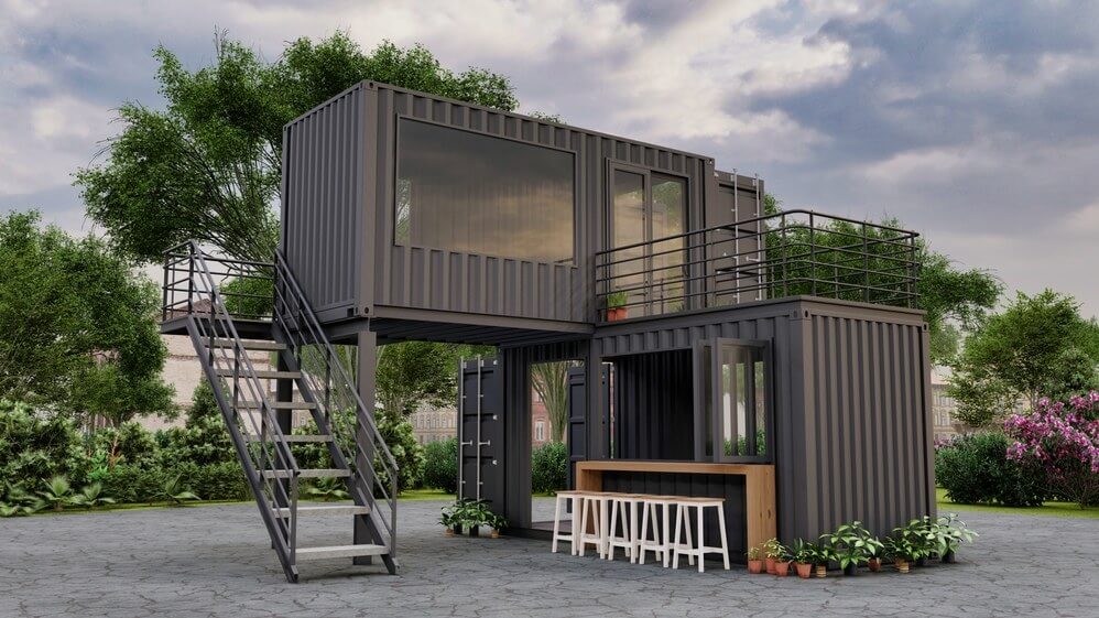 Small Black shipping container with stairs on the front side and small plants nearby with Glass window.